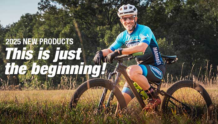 Hammer Athlete Sitting on mt bike smiling wearing a blue hammer kit in field.