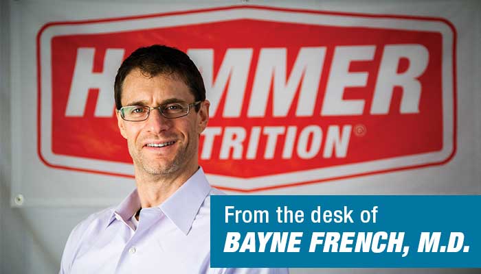 Dr. Bayne French smiling at camera with red Hammer Nutrition banner behind him.